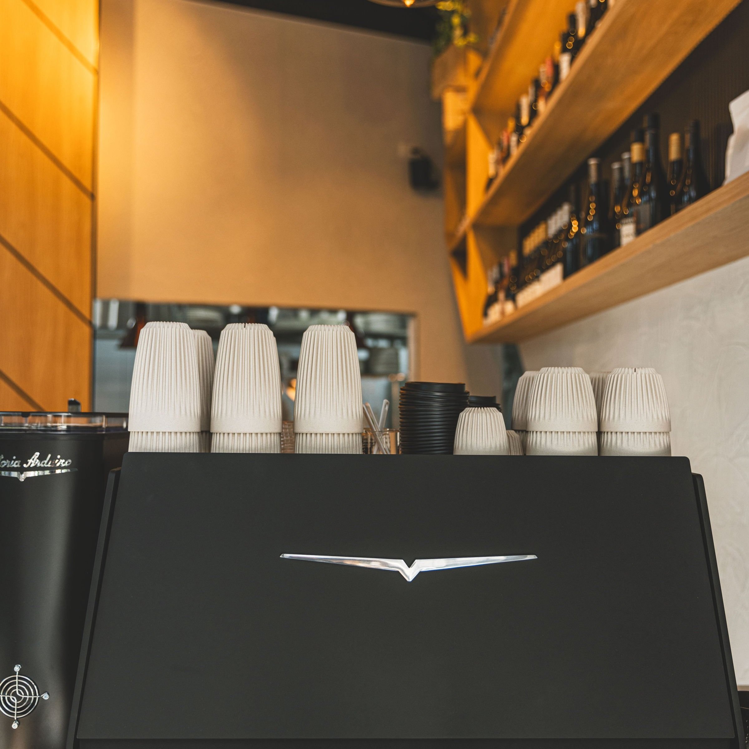 Thirty 7even's espresso machine with stacks of takeaway cups and a wall of bottled drinks behind